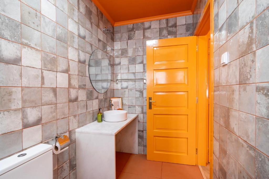 Bathroom with orange door and ceiling, gray tiled walls, white sink on a marble countertop, and toilet.