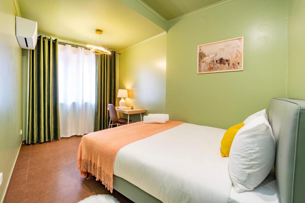 Bedroom with green walls, bed with white and yellow pillows, orange blanket, desk, chair, and window with curtains.