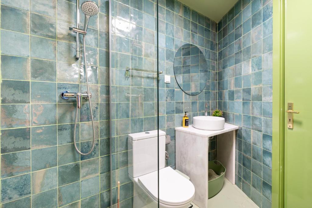 Bathroom with blue tiled walls, white toilet, small sink with round mirror, and glass shower screen.