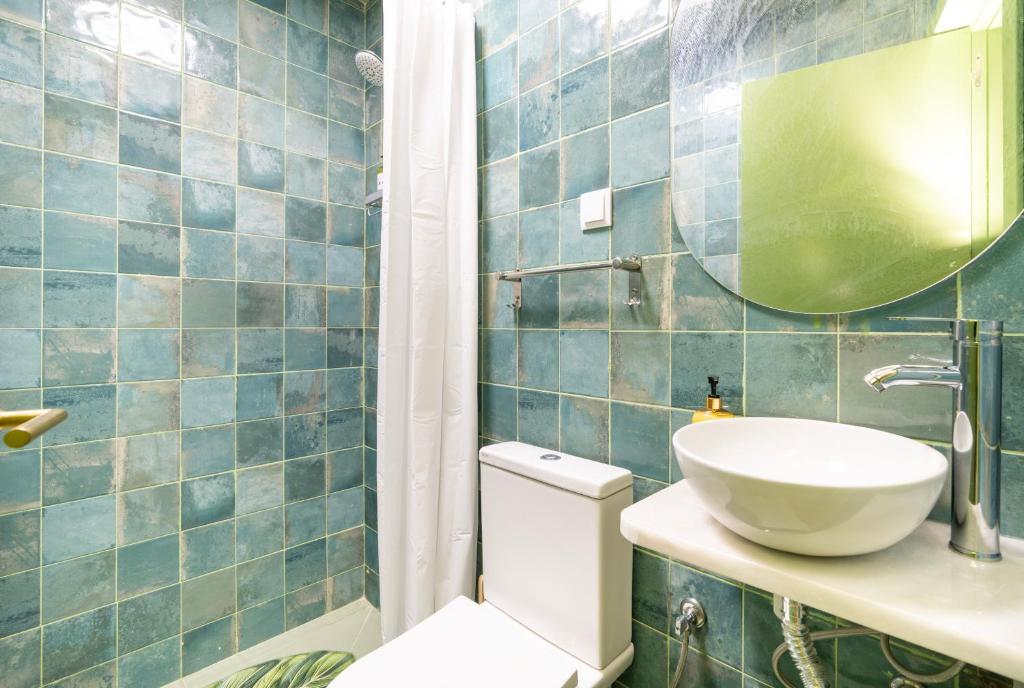 Bathroom with greenish-blue tiled walls, white toilet, white shower curtain, round mirror, and white sink bowl.