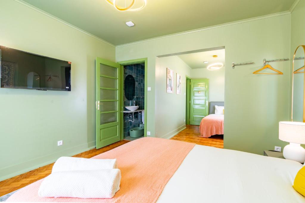 Bedroom with two beds, green doors, peach-colored blankets, TV mounted on wall, and bedside lamp.