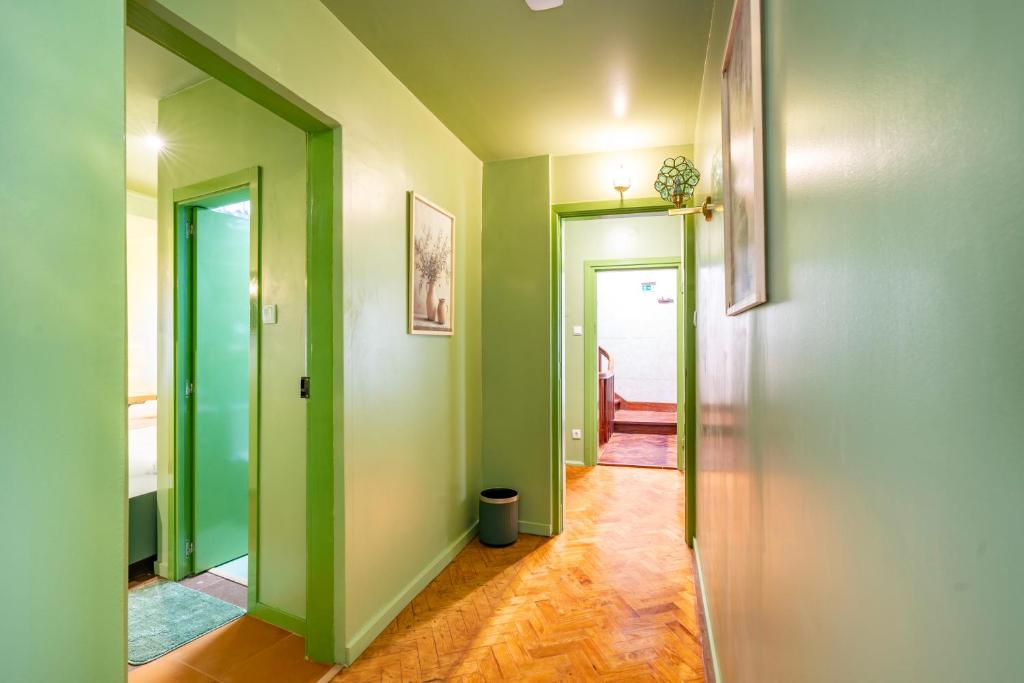 Hallway with green walls and door frames, wooden floor, a trash bin, and framed pictures on walls.