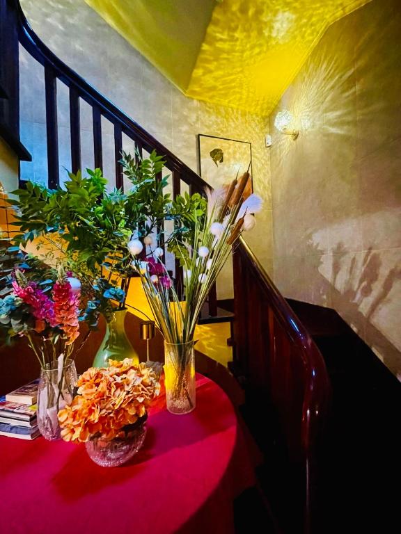Vase of flowers and plants on a red tablecloth near a wooden staircase with warm lighting.
