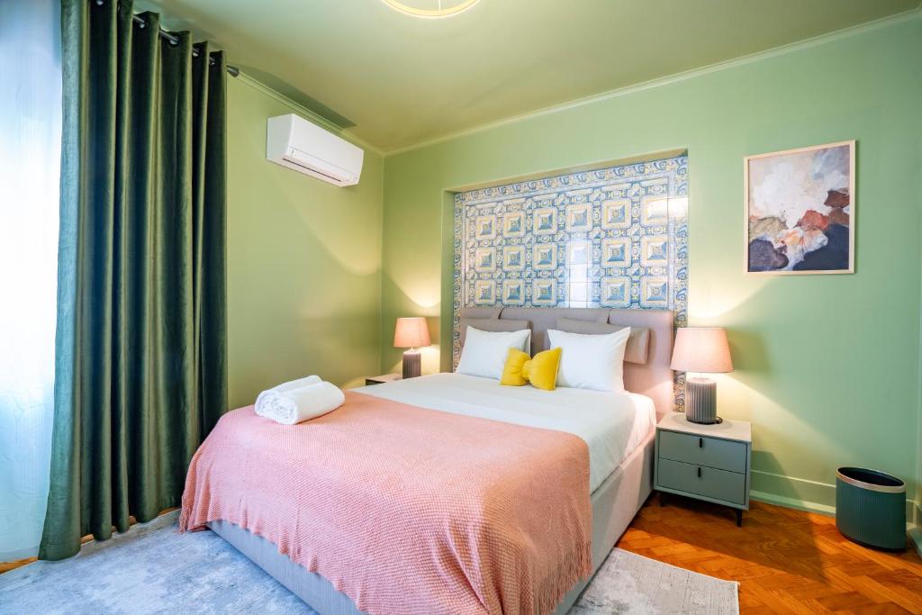 Bedroom with green walls, patterned tile headboard, pink bedspread, and two bedside lamps on gray drawers.