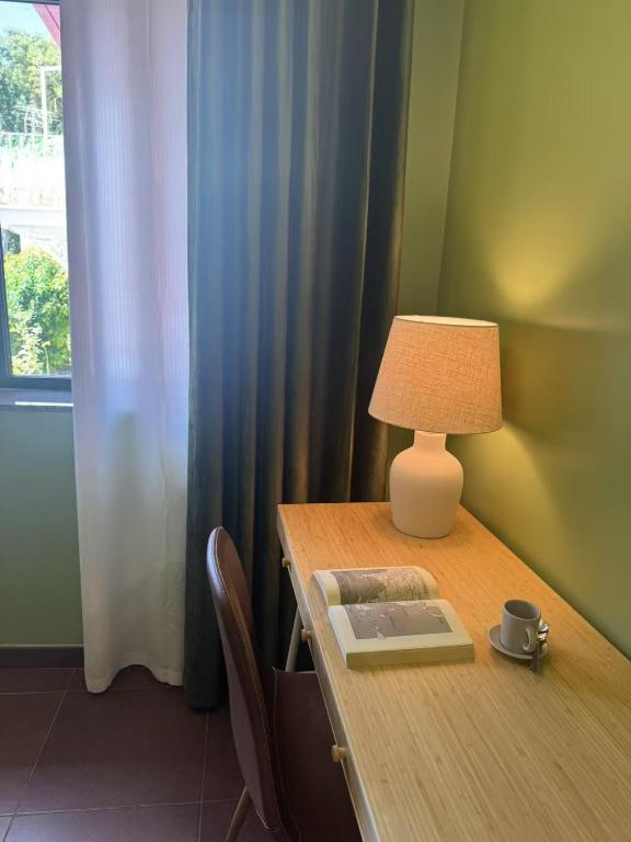Wooden desk with open book, lamp, coffee cup, and brown chair beside window with curtains.