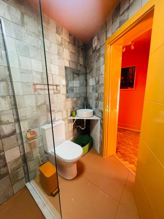 Compact bathroom with a white toilet, vessel sink, grey tiled walls, and an orange doorway.
