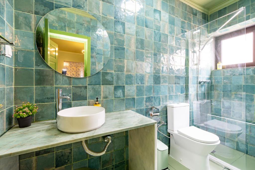 Bathroom with greenish-blue tiled walls, round mirror, white sink, toilet, and glass shower enclosure.