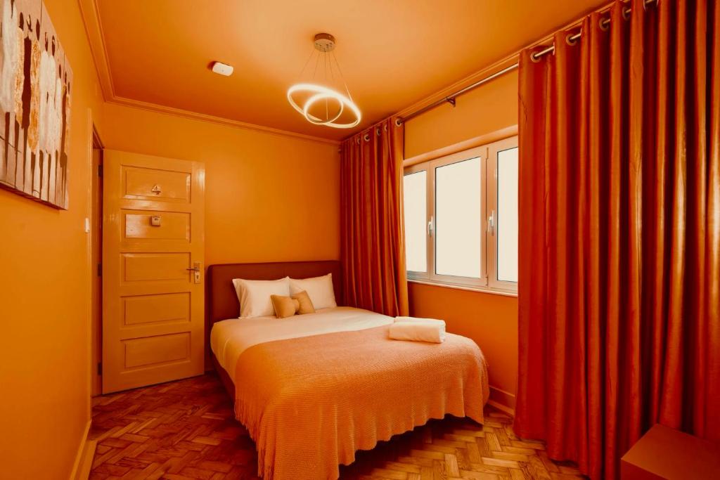 Cozy bedroom with orange walls and curtains, a double bed with white pillows, and modern ceiling light.