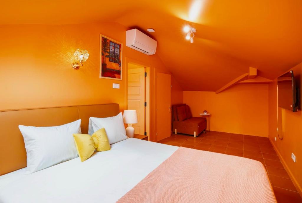 Bright orange bedroom with white and yellow pillows on bed, wall art, chair, and mounted TV.