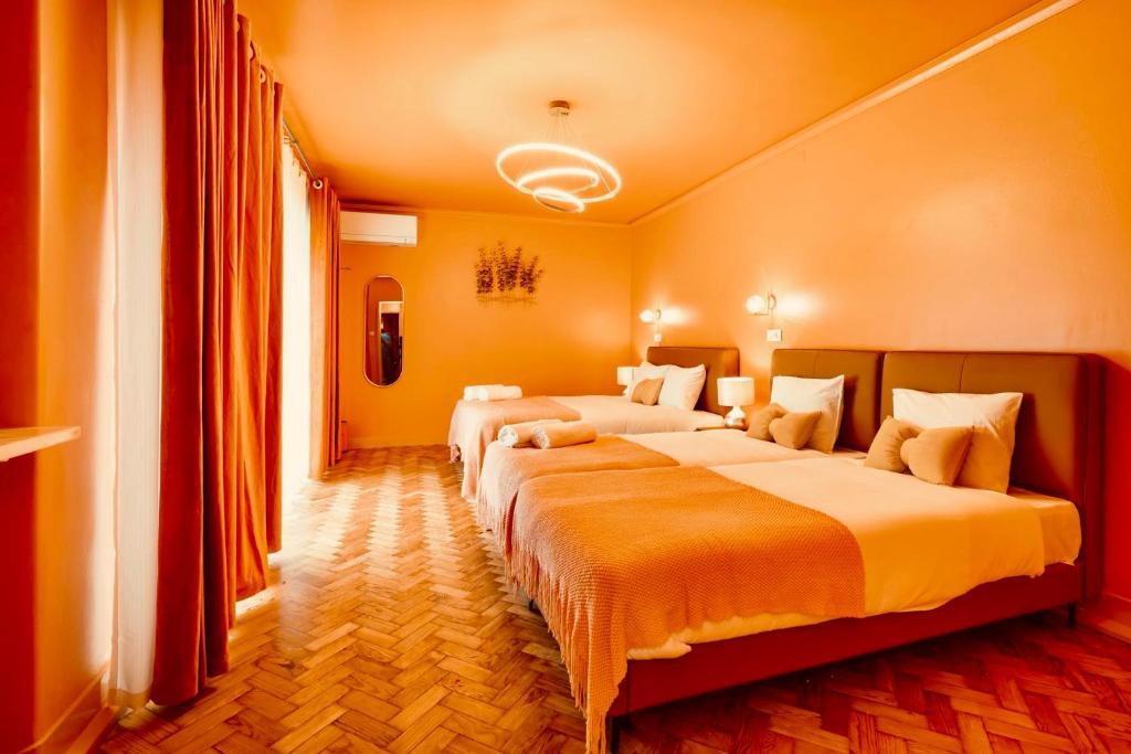 Bright orange-toned hotel room with two beds, orange curtains, modern ceiling light, and wooden parquet floor.