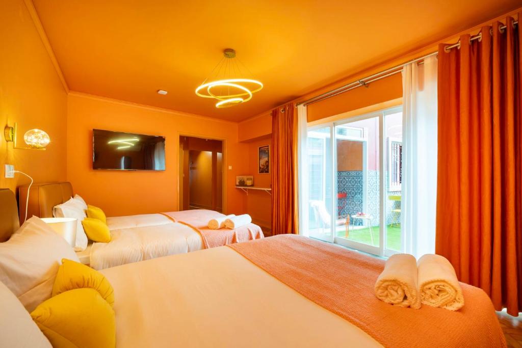 Bright orange bedroom with two beds, white and yellow pillows, a TV, and glass doors to a patio.