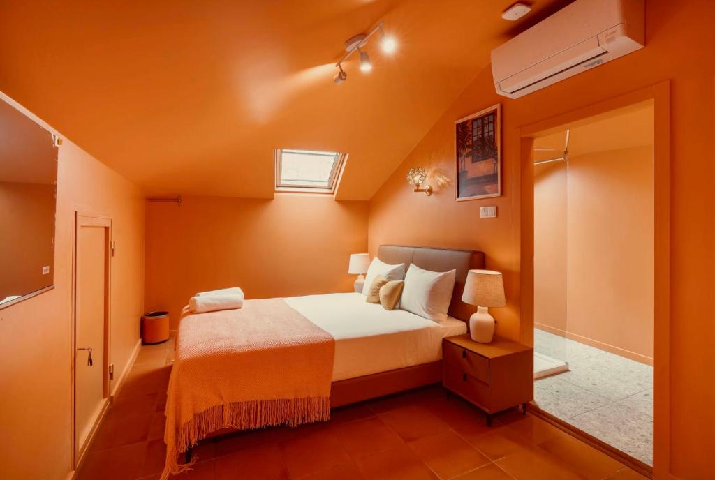 Cozy orange-toned bedroom with a bed, bedside tables, lamps, skylight, and air conditioner.