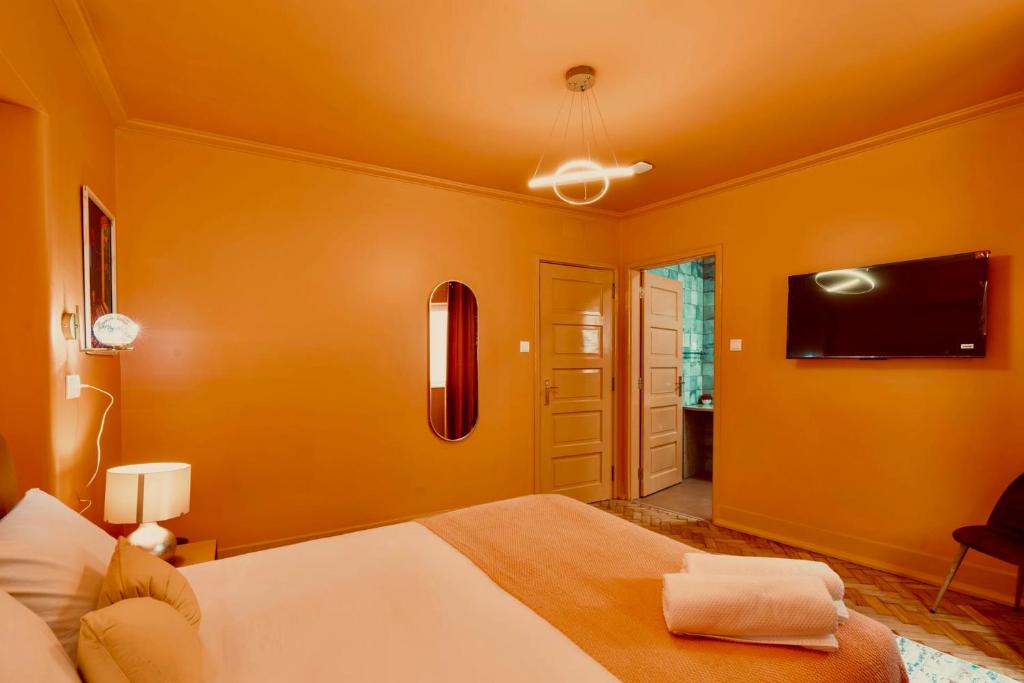Cozy orange bedroom with bed, folded towels, wall-mounted TV, and open door to bathroom.