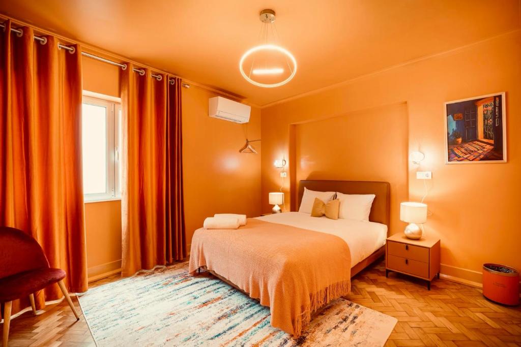 Cozy orange-themed bedroom with bed, bedside tables, lamps, curtains, chair, and artwork.