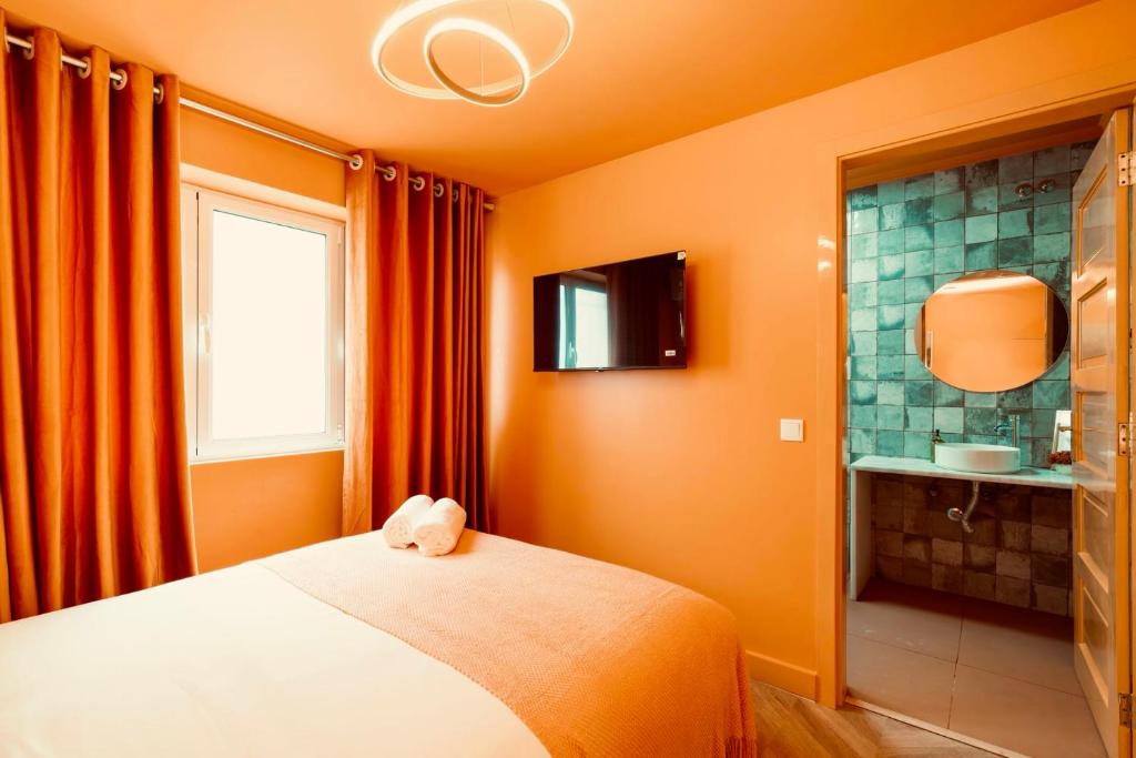Small bedroom with orange walls, bed with folded towels, mounted TV, and bathroom with green tiles.