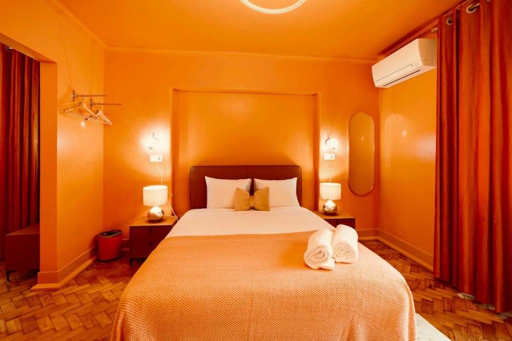 Orange-themed bedroom with bed, two pillows, bedside lamps, rolled towels, and wooden floor.