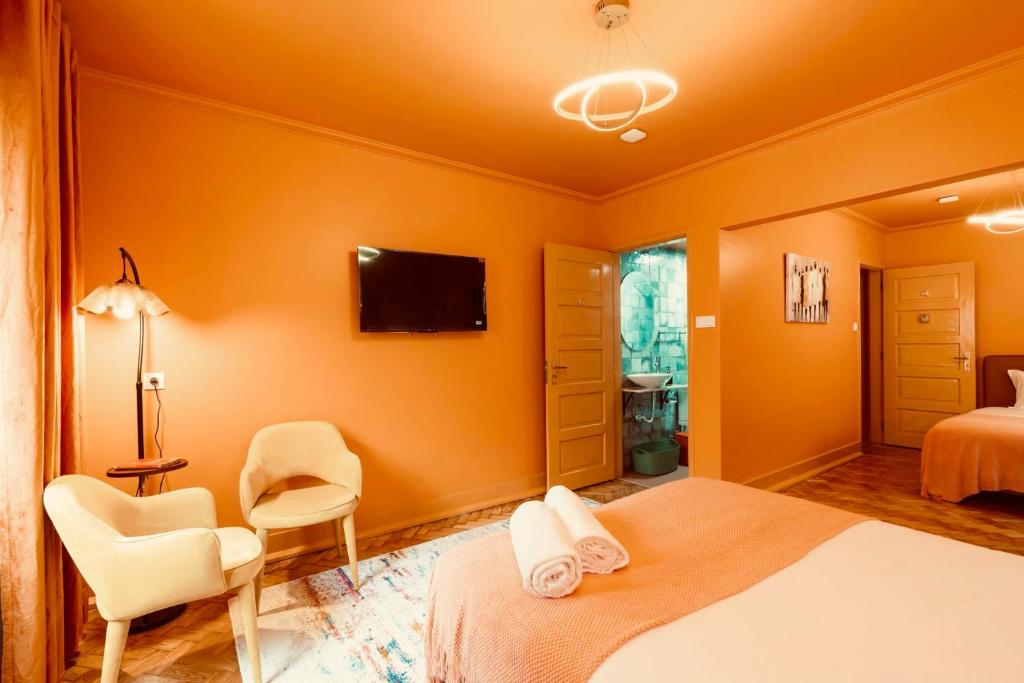 Cozy bedroom with peach walls, two beige chairs, wall TV, and a bed with towels on it.