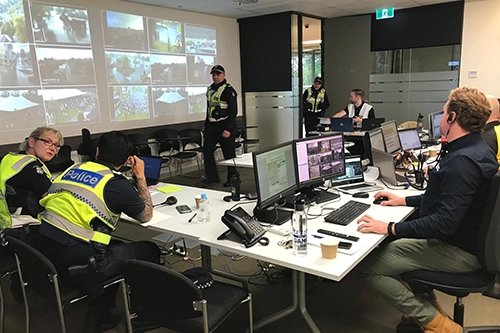 Police officers and staff monitoring multiple security camera feeds in a control room.