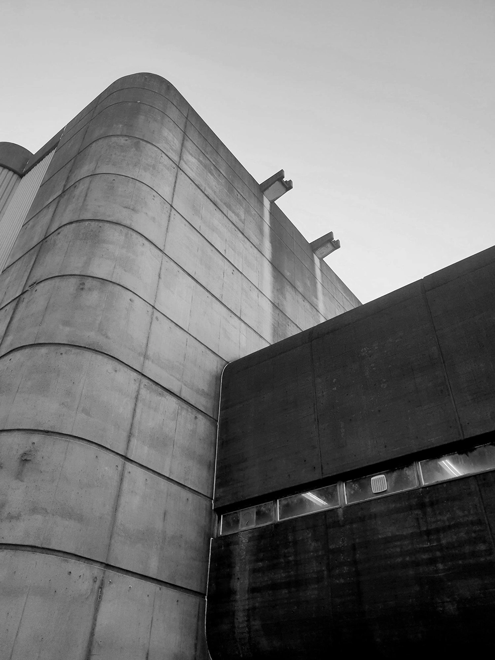 Upward view of a modern concrete building with rounded edges and horizontal lines on its facade under a clear sky.