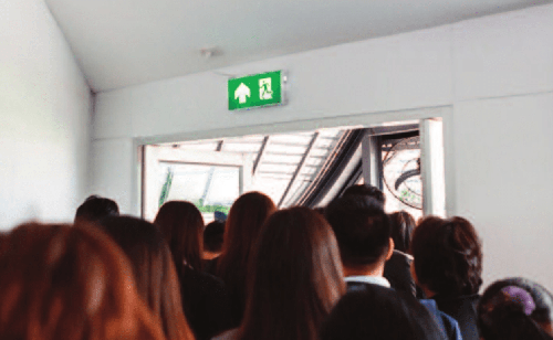 Crowd of people exiting through a door marked with a green emergency exit sign.