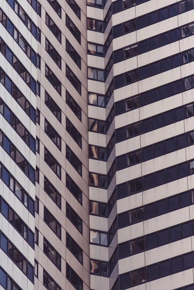 Close-up of a modern building facade with repetitive rows of dark windows and light panels forming a sharp corner.
