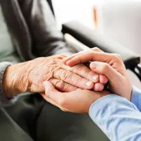 Junge Person hält liebevoll die Hände eines älteren Menschen.