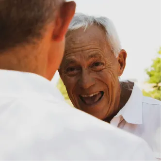 Älterer Mann lacht herzlich im Gespräch mit einer anderen Person im Freien.