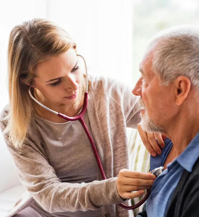 Ärztin hört mit einem Stethoskop die Brust eines älteren Mannes ab.