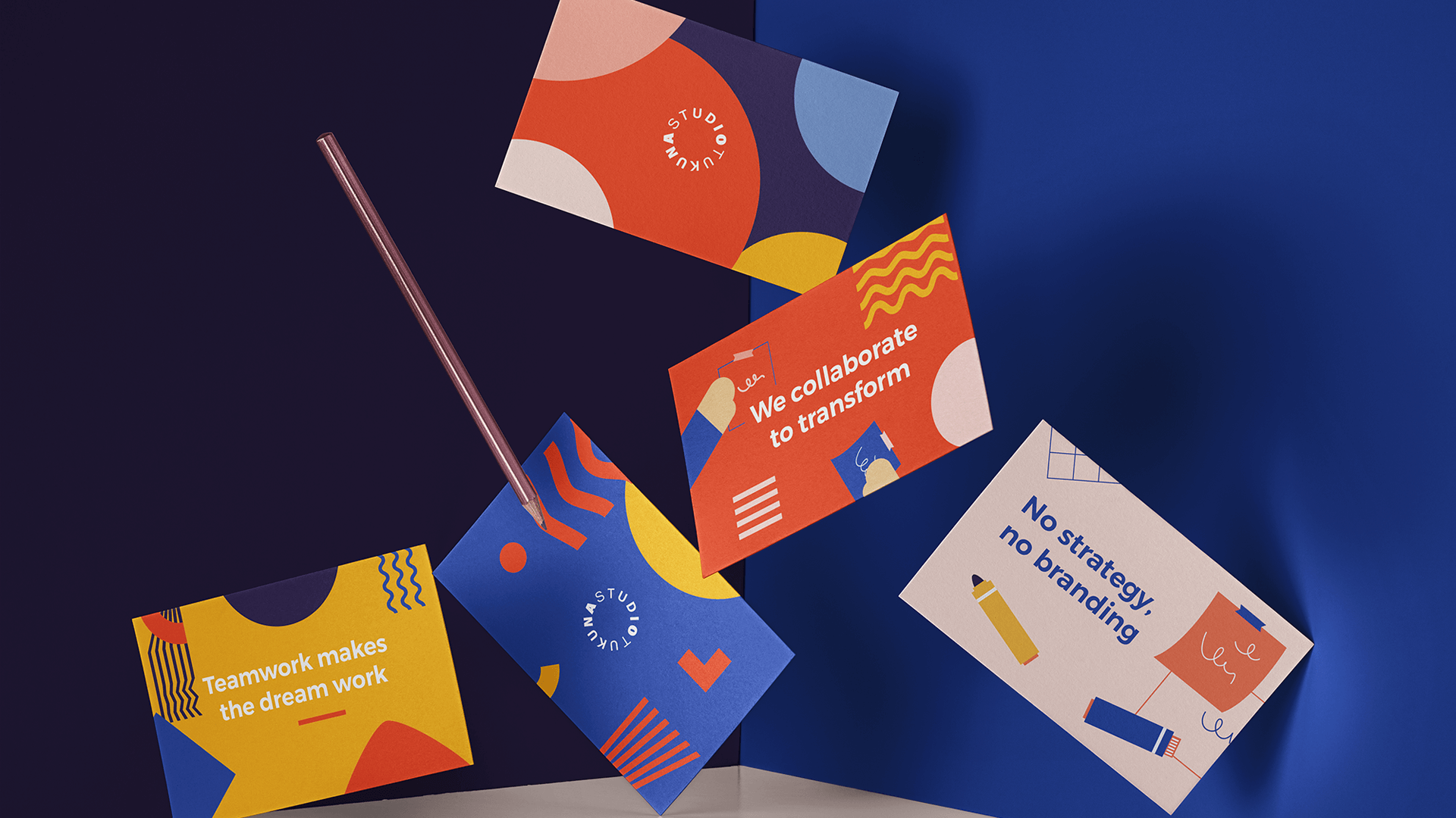 Five colorful Tukuna Studio postcards arranged with a pencil on a dark blue surface