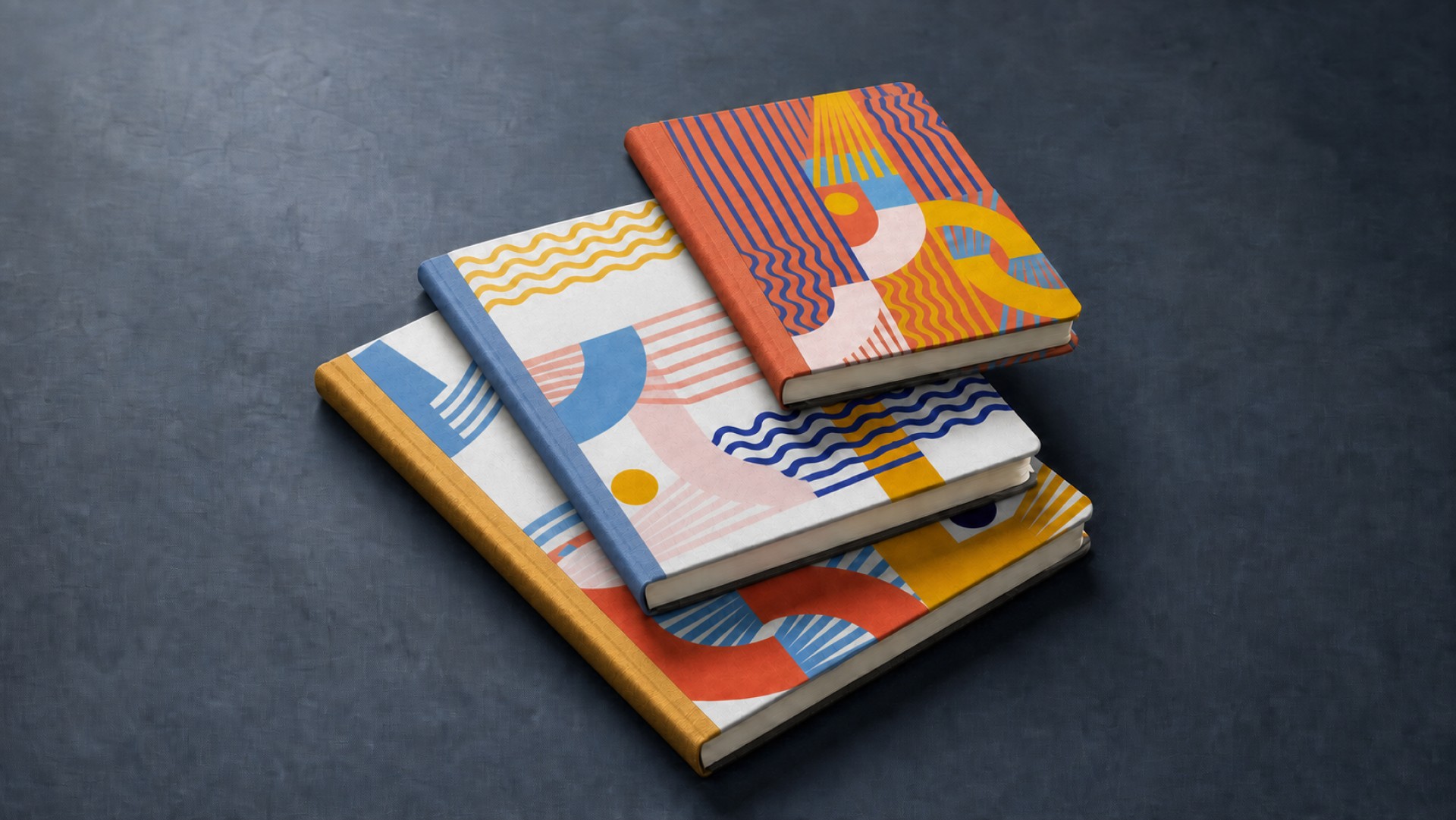 Stack of colorful Tukuna Studio hardcover notebooks on a dark surface