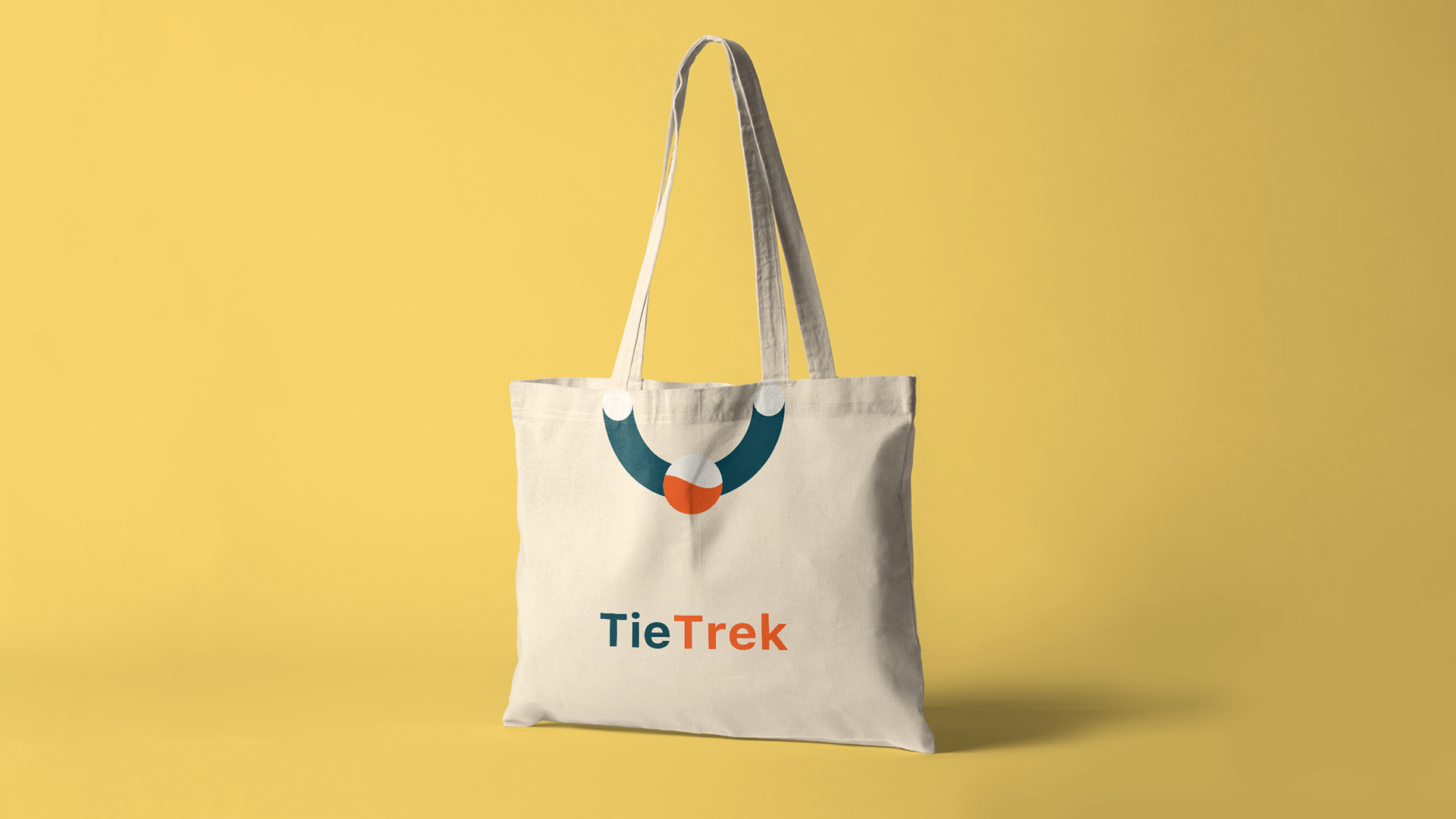 Cream TieTrek tote bag with teal and orange logo on a yellow background