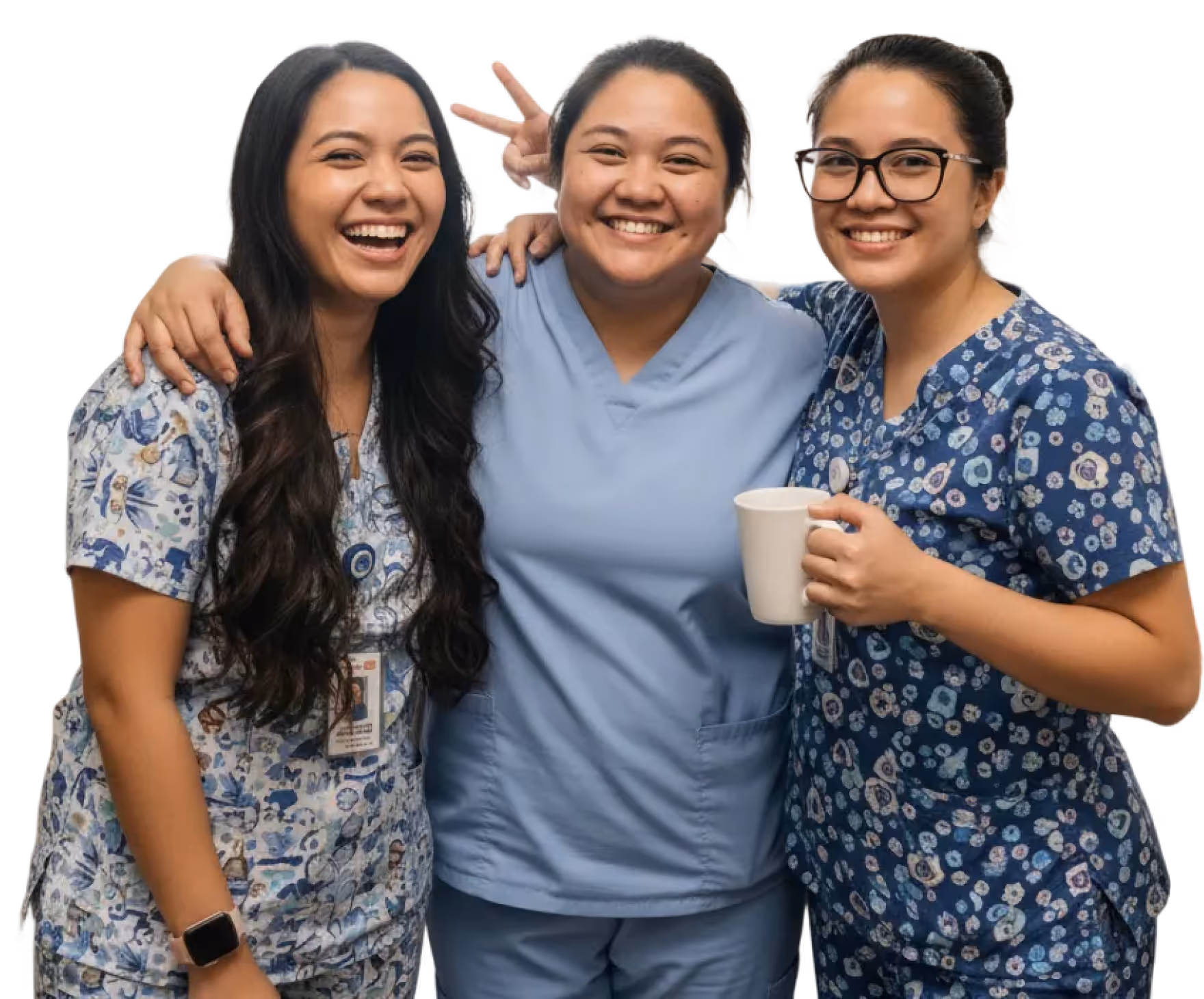 Three smiling female healthcare workers in scrubs posing together, one holding a cup and another making a peace sign behind the center person.