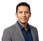 Portrait of a man wearing a gray blazer and dark blue shirt, smiling slightly against a plain background.