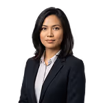 Professional woman with black hair wearing a dark blazer and white shirt against a black background.