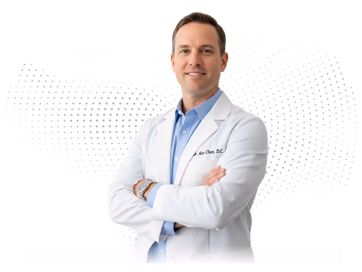 Confident male doctor wearing a white coat and blue shirt with arms crossed, smiling at the camera.