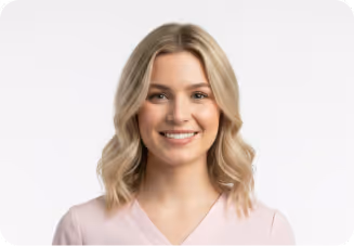 Smiling young woman with wavy blonde hair wearing a light pink top against a white background.