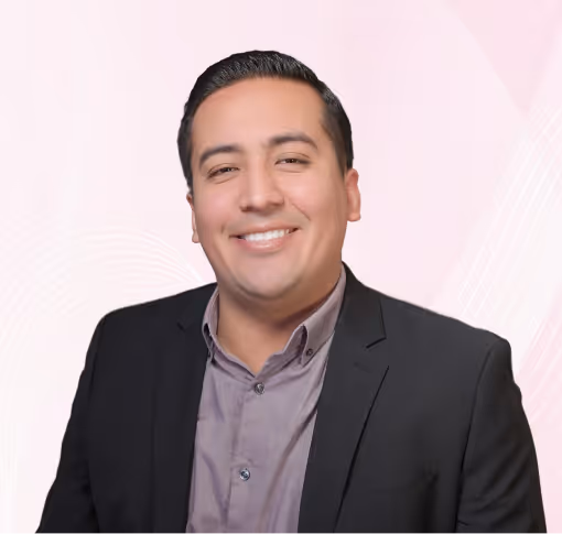 Smiling man with slicked-back dark hair wearing a black blazer and light purple shirt against a blue abstract background.