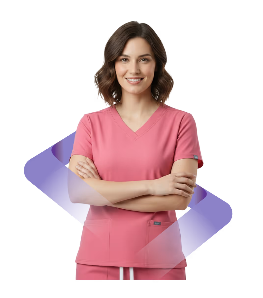 Smiling woman in pink medical scrubs with arms crossed, standing against a white background.