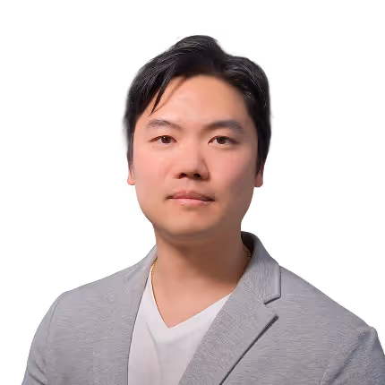 Portrait of a man with black hair wearing a gray blazer and white shirt against a transparent background.