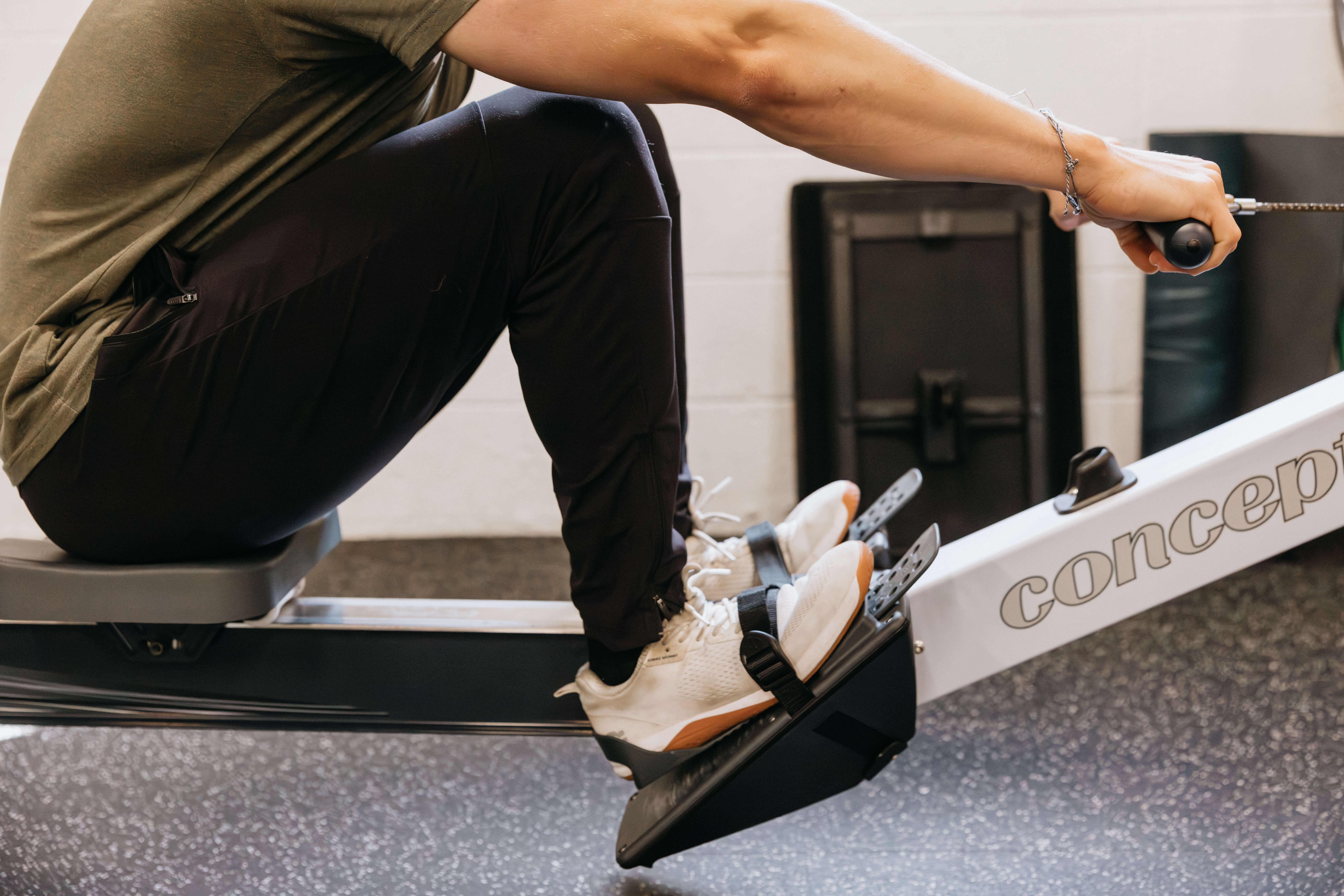 Person using a rowing machine with feet strapped to footrests and hands gripping the handle.
