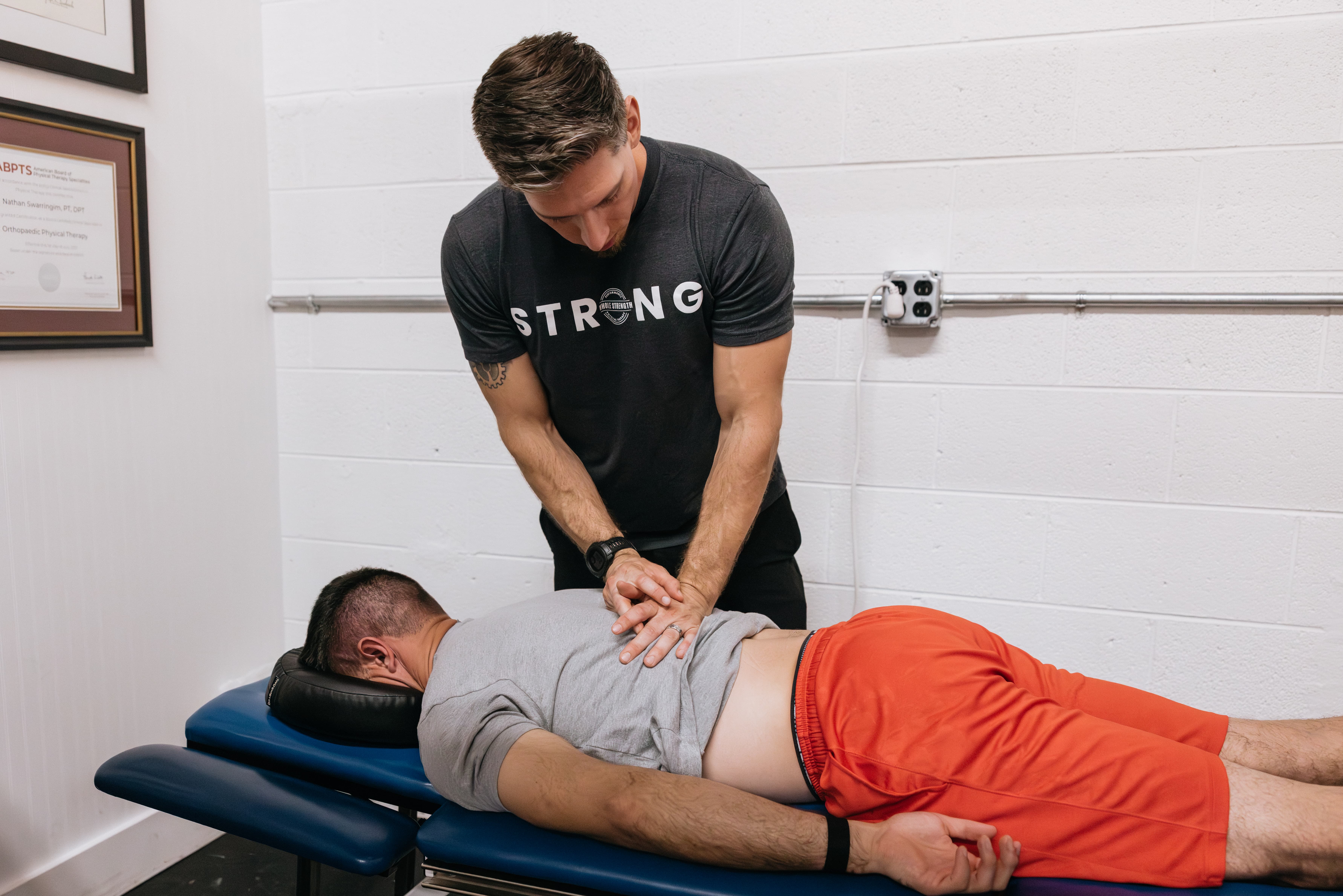 Therapist in a strong t-shirt doing treatment on a patients back on the treatment table