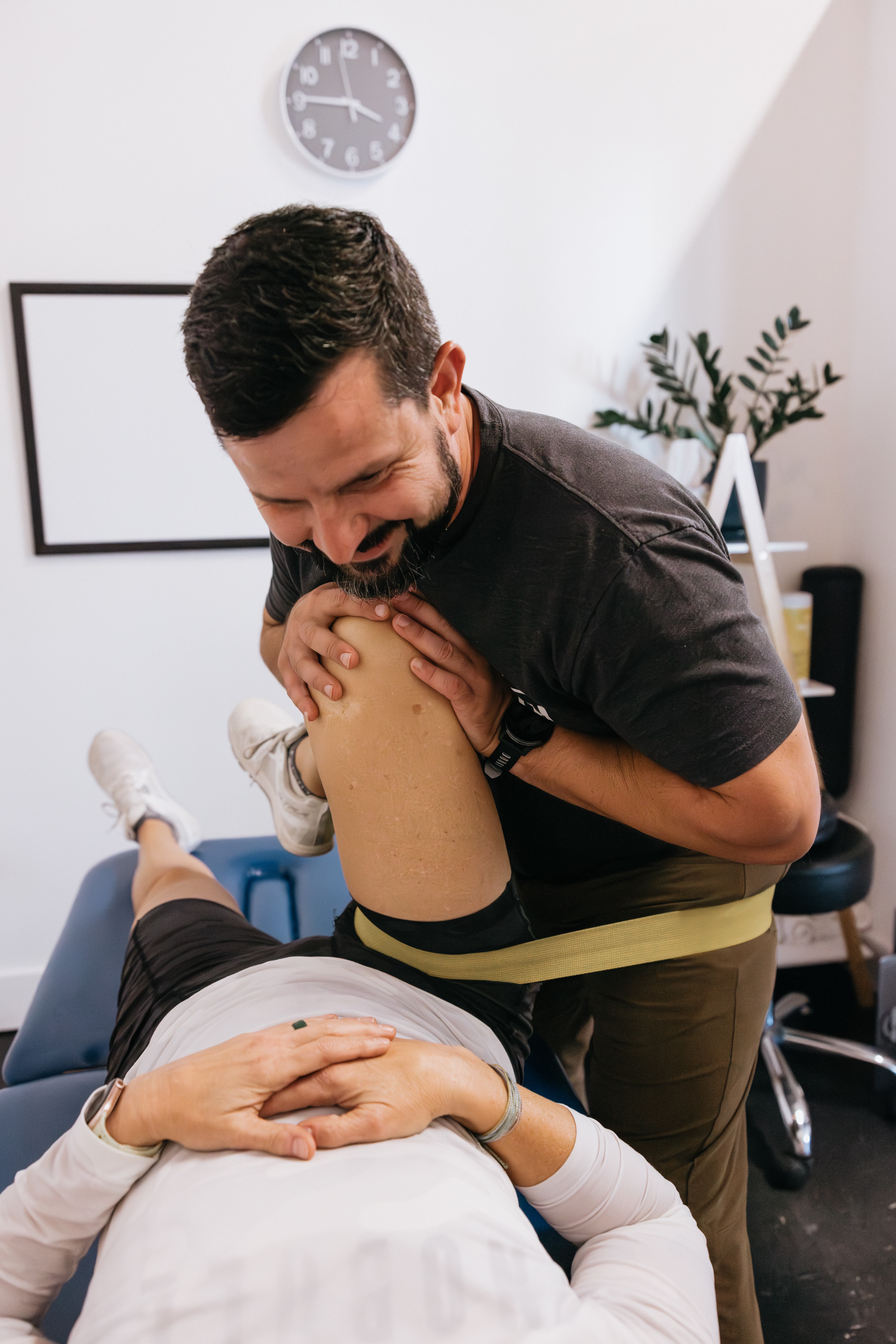 Therapist has a band around patient with a raised knee and leg stretching on the treatment table