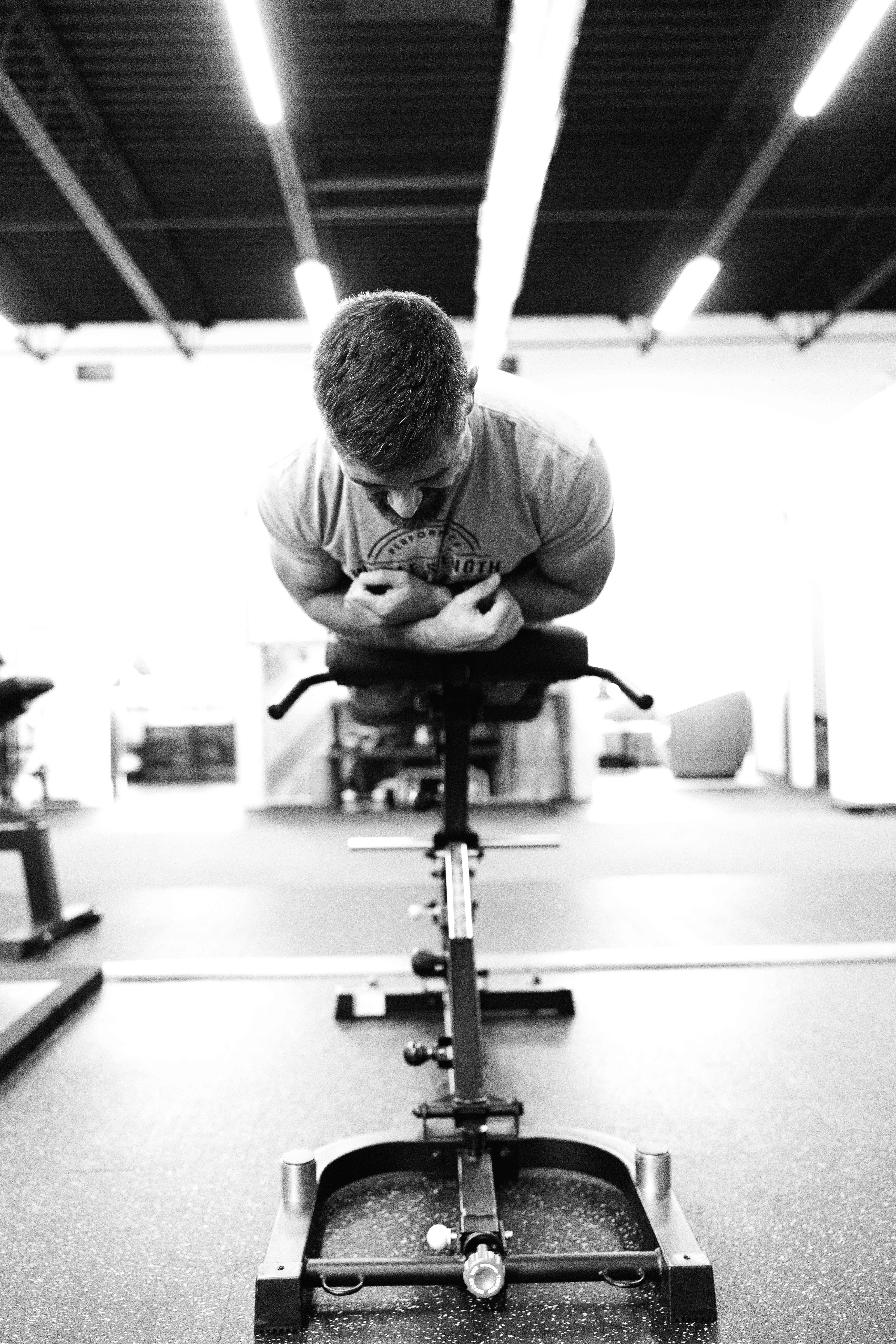 Black and white photo of man facing forward looking down doing a back hold on a machine