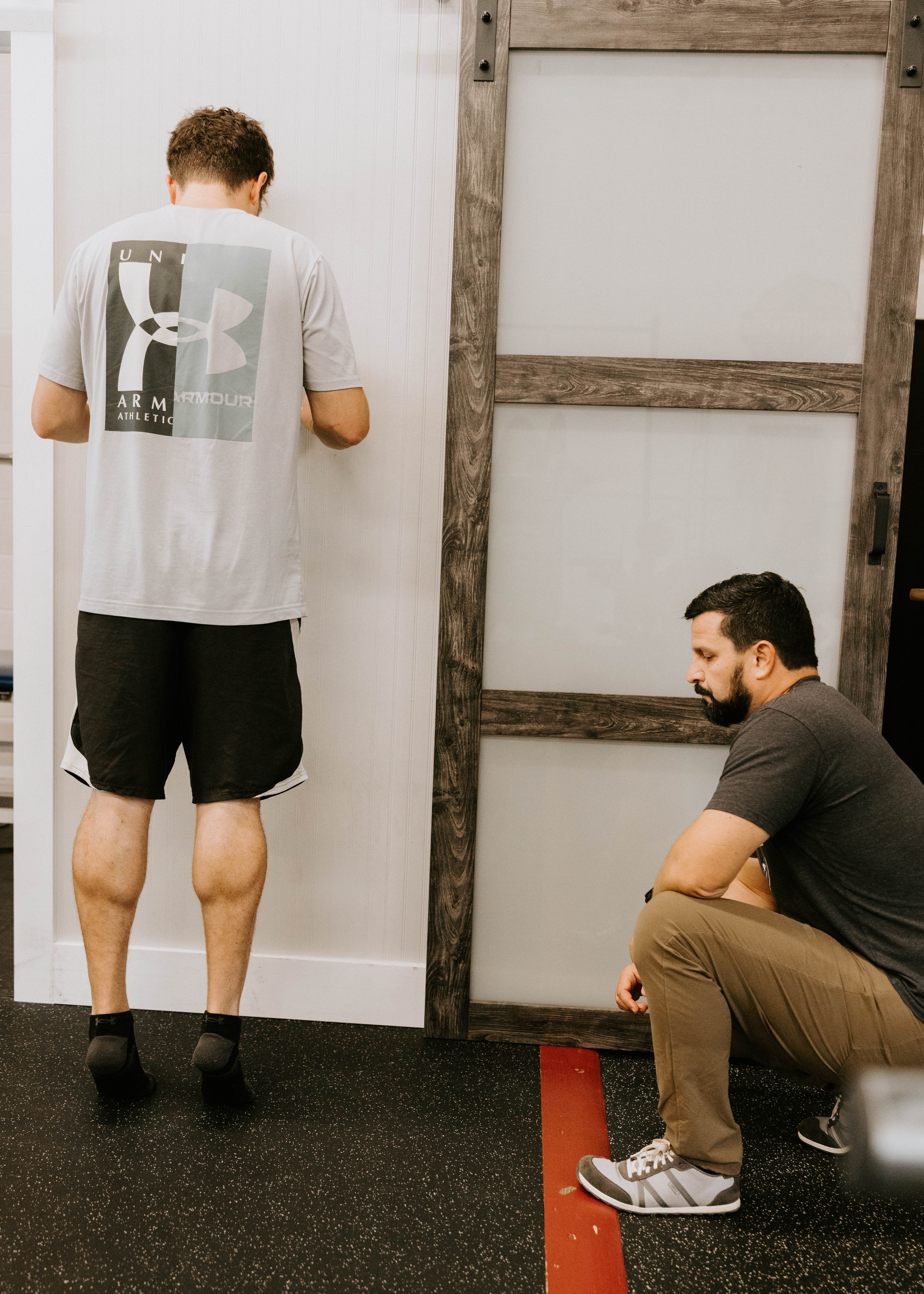 Photo of patient sitting on a treatment table with arms crossed while therapist is behind him holding his arms and helping him rotate. 