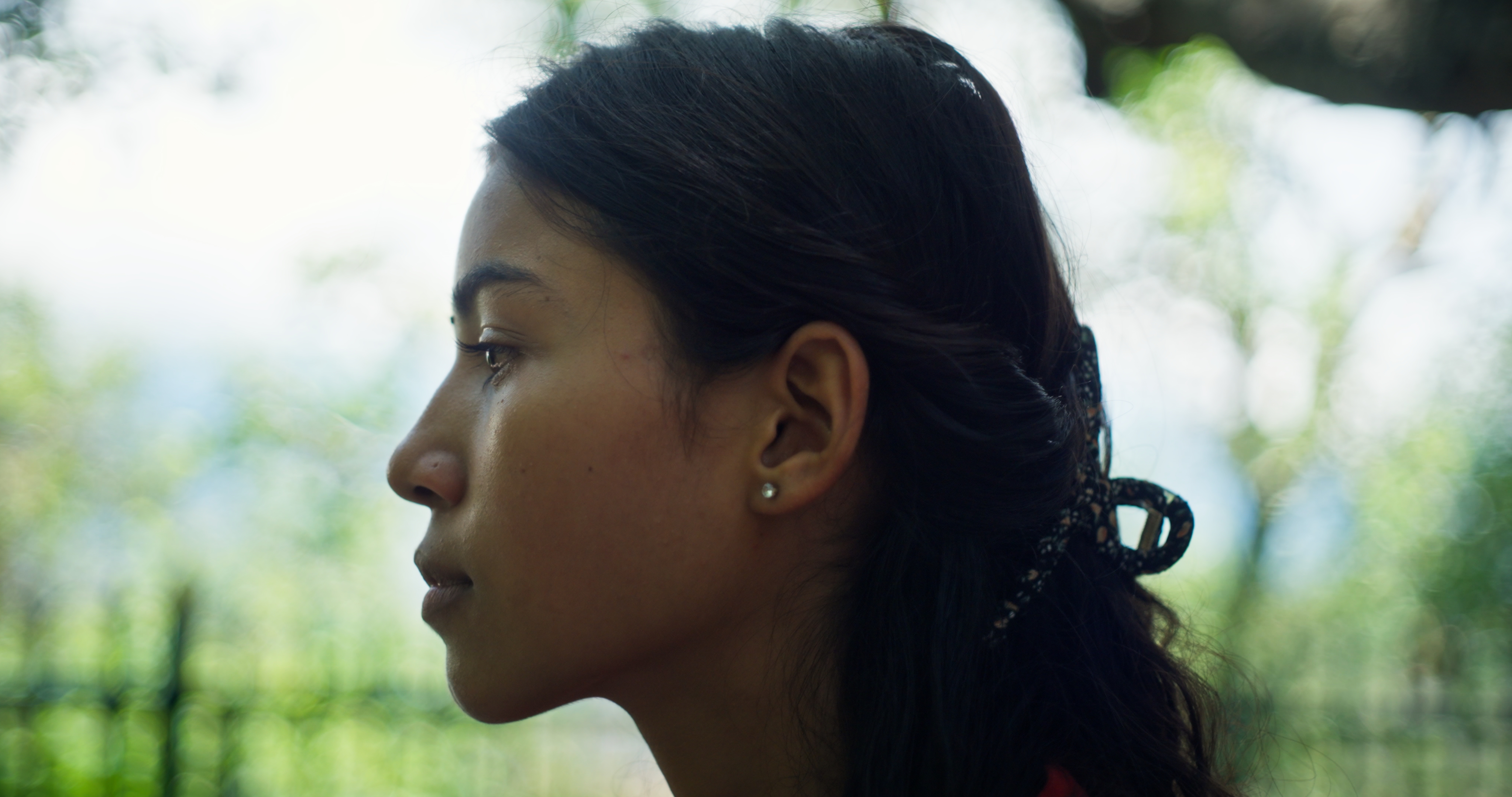 Side profile of Tikaram's sister against a blurred green outdoor background.
