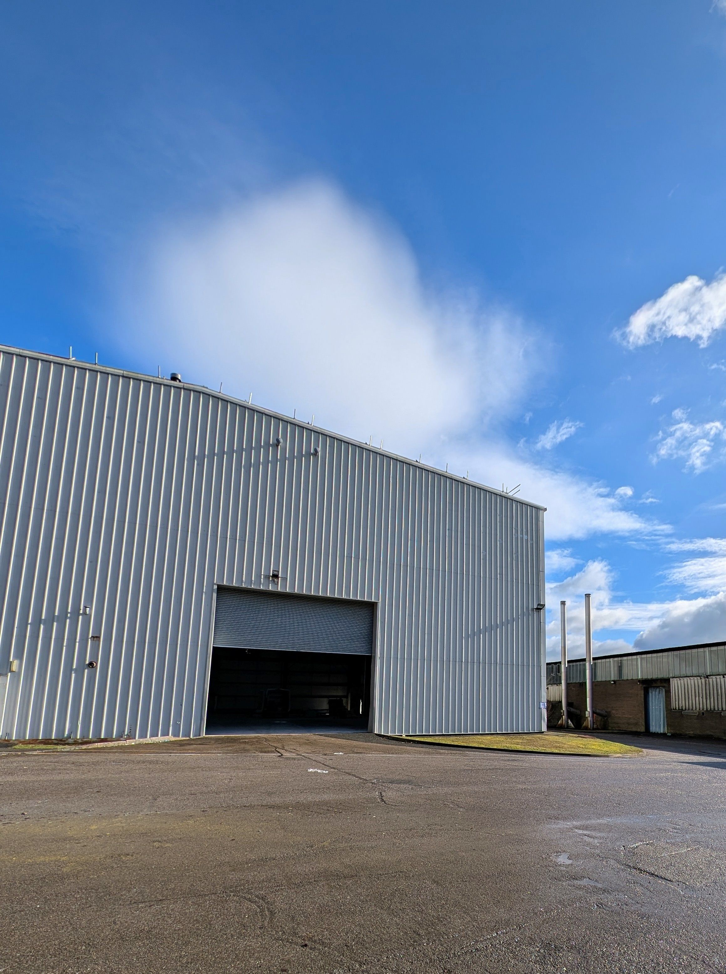 Unbound padel club in a large industrial warehouse with a partially open roller door under a blue sky with some clouds.