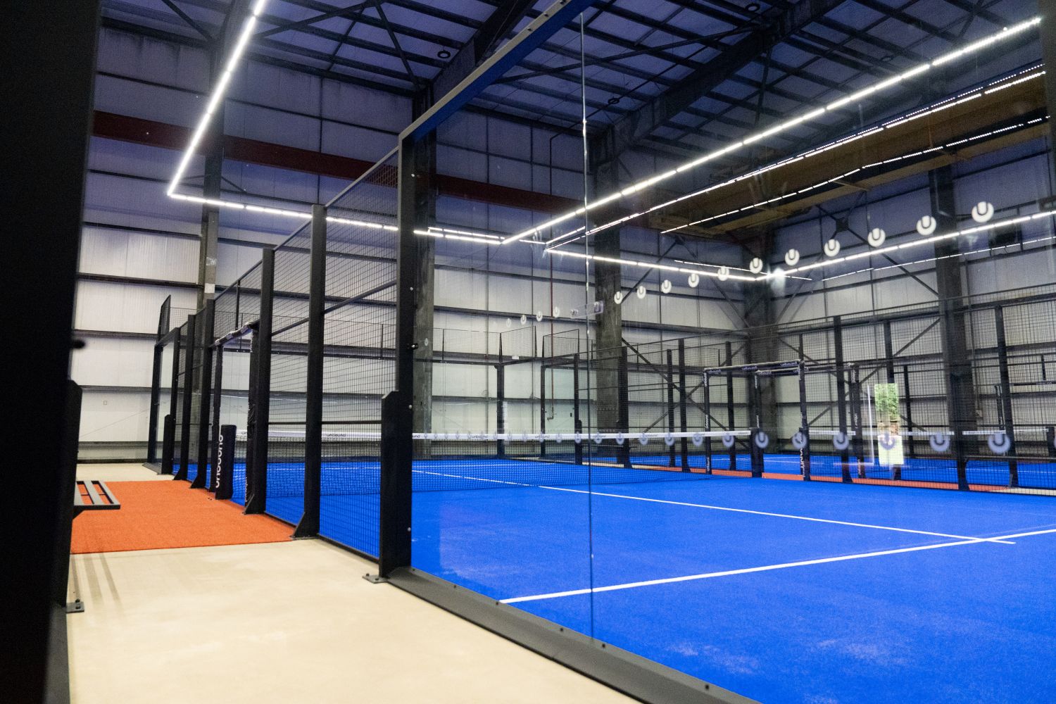 Spacious empty industrial warehouse with high ceiling, bright overhead lights, and a yellow overhead crane ready for new padel club