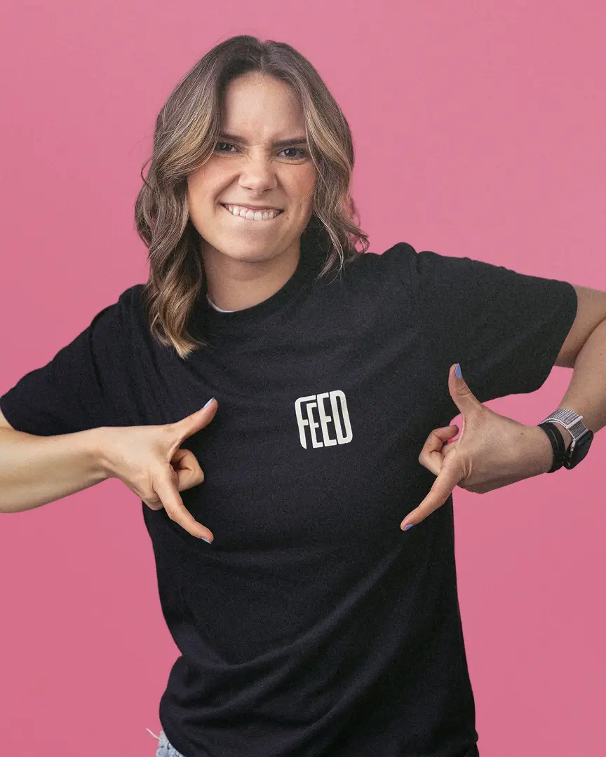 Emma making a playful face and pointing at the word 'FEED' on her black t-shirt.