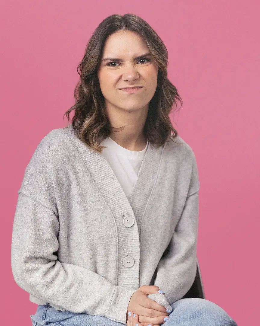 Emma wearing a gray cardigan and light blue jeans, making a scrunched-up face.