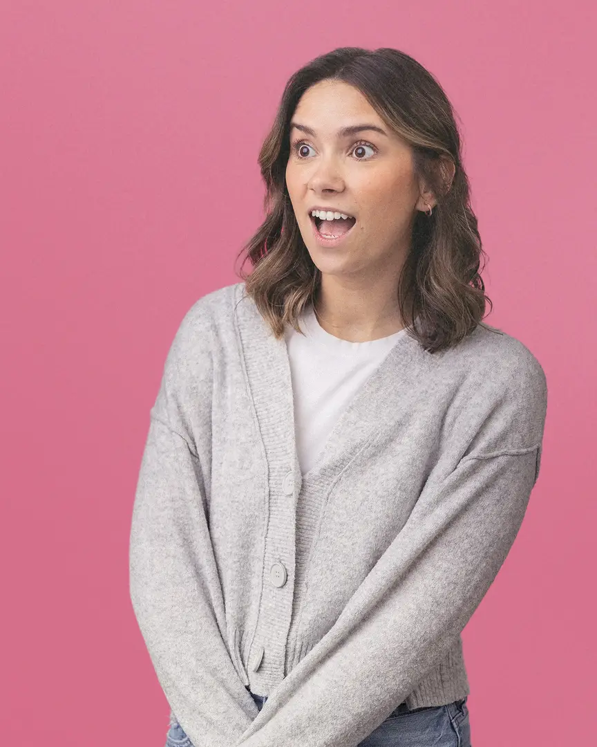 Emma wearing a gray cardigan and white shirt, looking surprised.